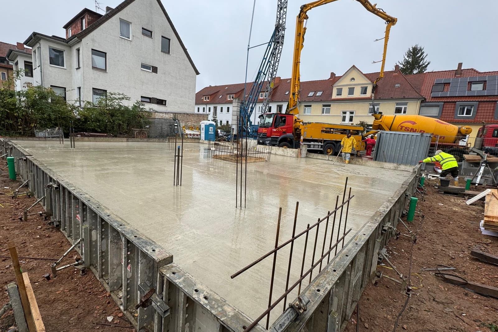 Betonpumpe beim Betonieren einer Bodenplatte zwischen Bestandshäusern, die Schalung und Anschlussbewehrung sind zu sehen